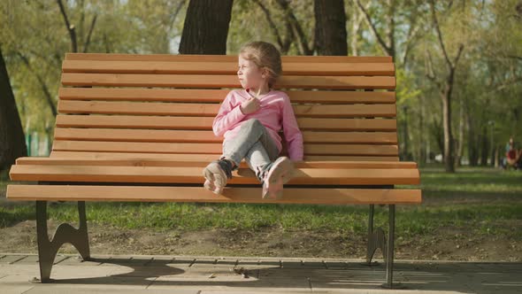 Little Girl Suffers From Hot Weather Sitting on Park Bench