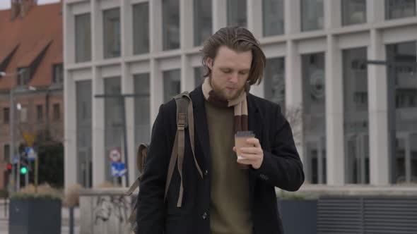 stylish guy in scarf and coat with takeaway cup of coffee at street of Wroclaw, Poland