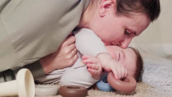 The mother kisses the happy laughing baby and hugs him. Mom amuses a smiling, happy child, age eight