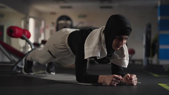 Portrait of Endurant Middle Eastern Sportswoman in Plank Position on Exercise Mat Indoors