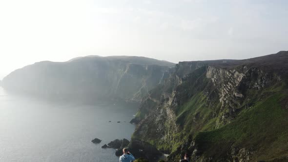 Two people sitting on the cliff edge looking at the mountain range at Horn Head in Donegal Ireland