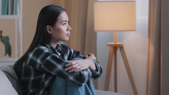 Side View Sad Asian Woman Sitting on Couch at Home Feeling Unsure About Hard Decision Unhappy Bad