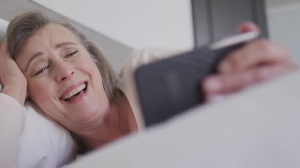 Woman having a video chat on her smartphone in bed at home