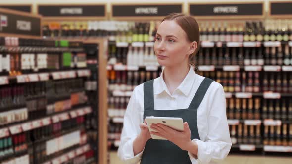 Young Manager Checks Bottles Typing on Tablet Closeup