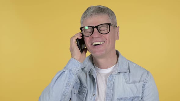 Casual Senior Man Talking on Smartphone on Yellow Background