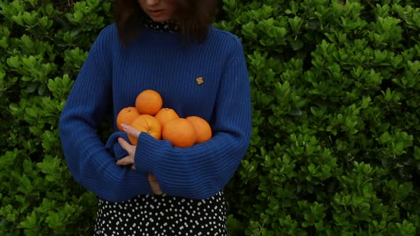 A Girl in a Blue Sweater Holds Ripe Oranges