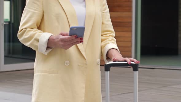 Business Woman with a Suitcase Uses a Mobile Phone and is Waiting for Someone