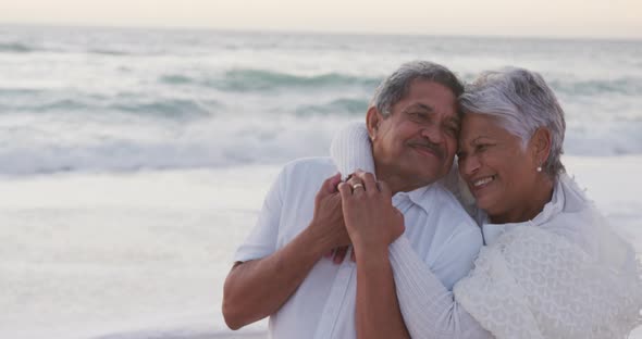 Happy hispanic just married senior couple embracing on beach at sunset