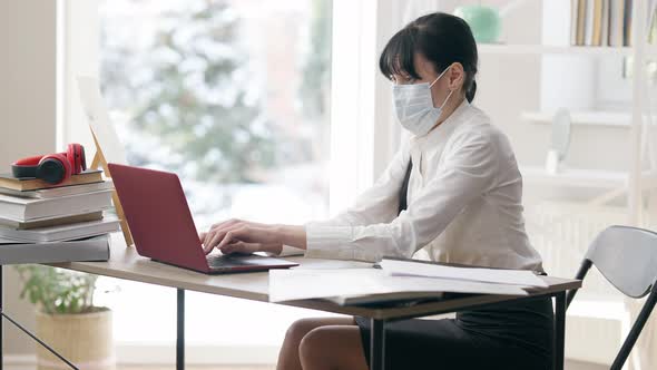 Side View of Ill Young Woman in Covid Face Mask Sneezing Typing on Laptop Keyboard