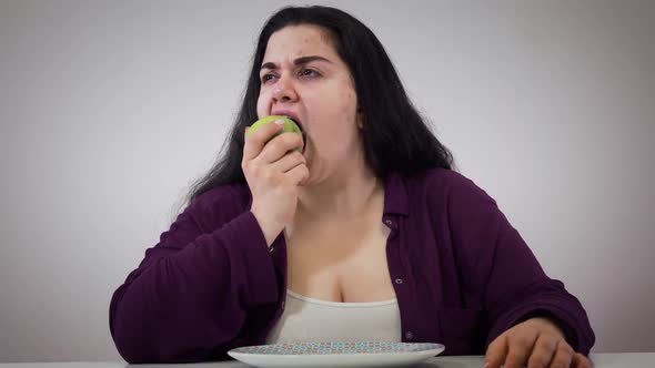 Portrait of Young Plump Caucasian Woman Taking Apple and Signing, Upset Fat Girl Eating Healthy Food