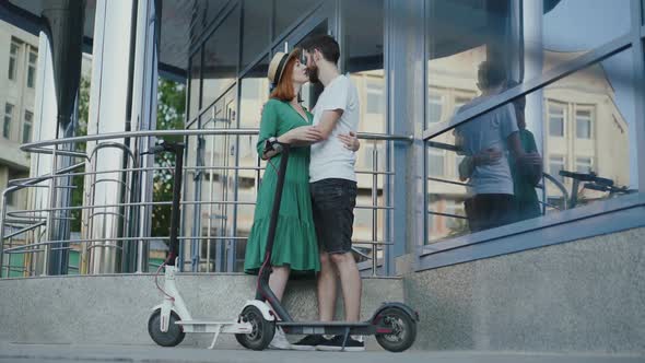 Couple in Love Embraces and Kisses Each Other at Office Centre Near Scooters