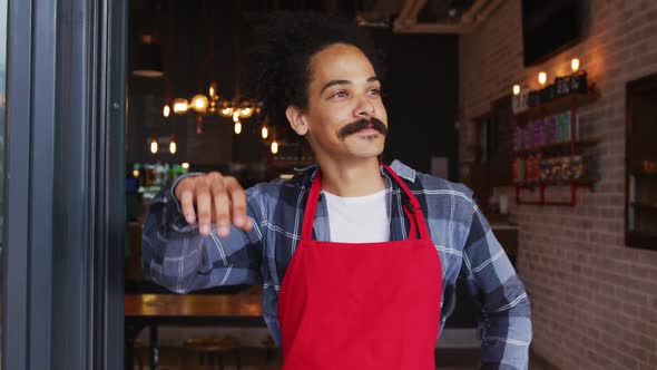 Mixed race male barista with moustache leaning in the doorway of cafe smiling