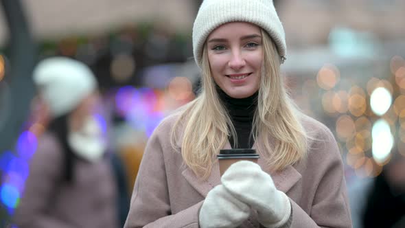 young girl walking with a cup of hot coffee on the background of Christmas lights