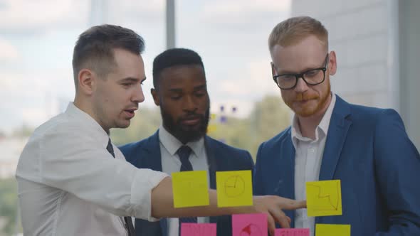 Diverse Young Businesspeople Discussing Marketing Plan and Making Notes on Stickers