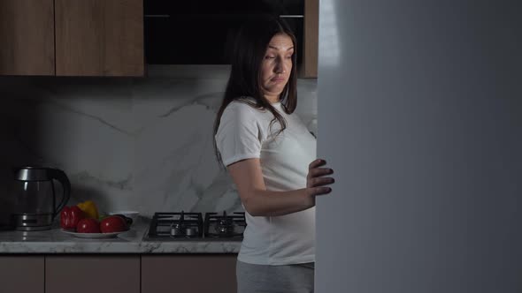 Pregnant Brunette Woman Eats Greenery in Kitchen at Night