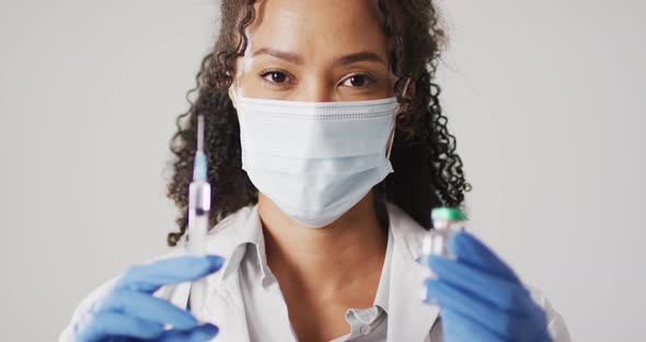 Video of portrait of biracial female doctor with face mask holding vaccine vial on white background