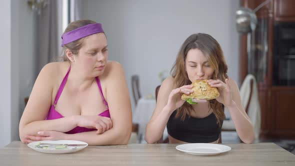 Jealous Fat Woman Looking at Slim Caucasian Friend Eating Sandwich