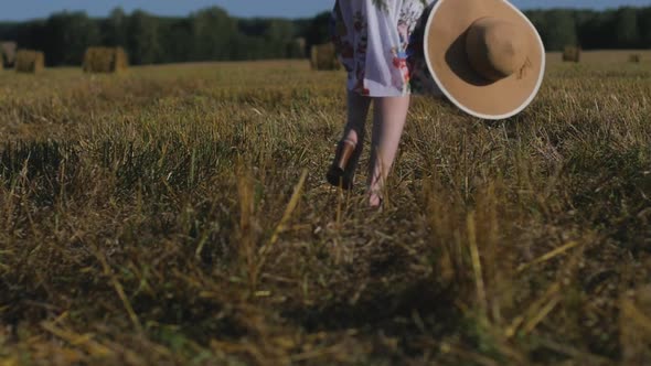 Woman in White Dress Closeup Holds Hat in Her Hands on Background of Field