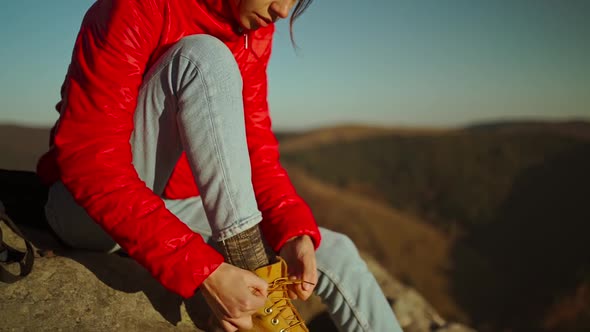 Slow Motion Adventurous Female Hiker Backpacker in Red Jacket with Backpack Sits on Cliff Top at