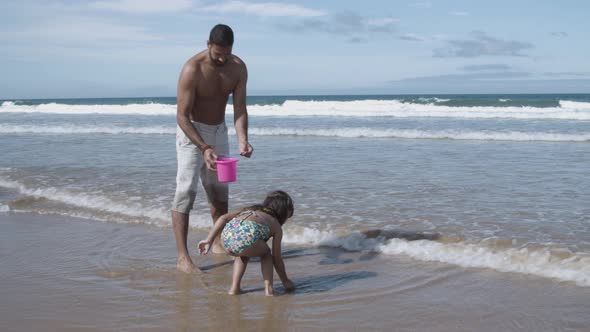 Little Girl and Her Dad Picking Shells Into Bucket