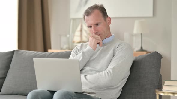 Middle Aged Businessman Thinking and Working on Laptop on Sofa