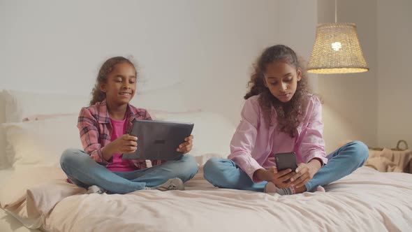 Elementary Age Girls with Gadgets Resting on Bed