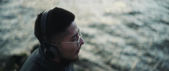 A guy listening music next to the river and slowly moving his head