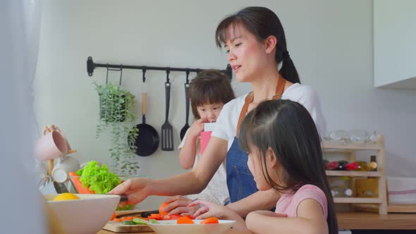 Loving beautiful Asian busy mother talk on phone and cooking with daughters in kitchen at home.