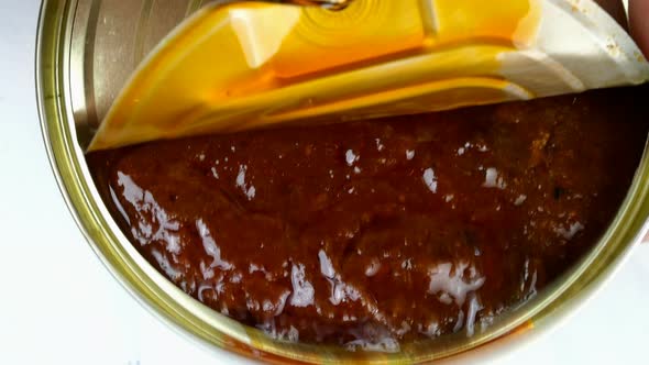 Hand Opens Metallic Tin Can of Canned Sardines or Mackerel in Tomato Sauce