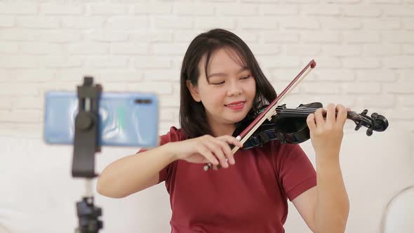 Asian female teacher teaching students how to play classical instrument violin from home