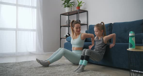 Young Woman and Her Primary School Age Daughter Are Doing Physical Exercises Together in Living Room