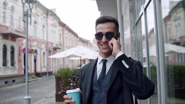 Businessman in Sunglasses Drinks a Cup of Beverage and Talking on Smartphone