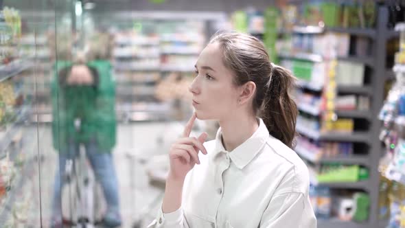 A Girl Shopper Looks at the Refrigerator with Food in the Supermarket