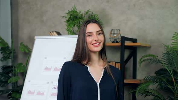 Smiling woman business coach turns head looking camera on background flip chart