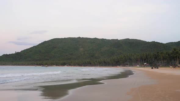 Small waves washing up on a long sandy beach with palm trees in the Philippines. Handheld camera