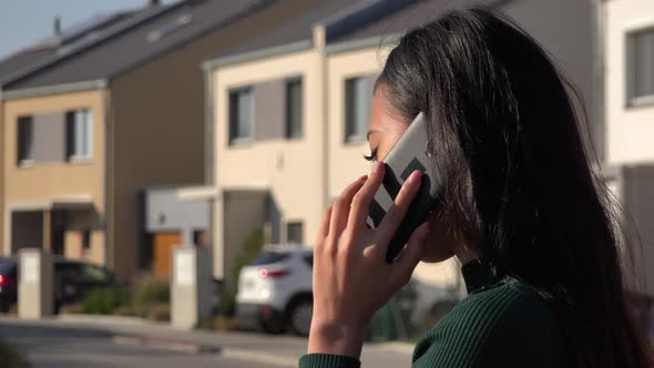 An Asian Woman Talks on A Smartphone in A Suburban Area on A Sunny Day