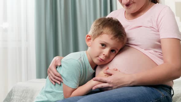 Portrait of Little Toddler Boy Hugging and Listening To Future Baby in Pregnant Mothers Belly