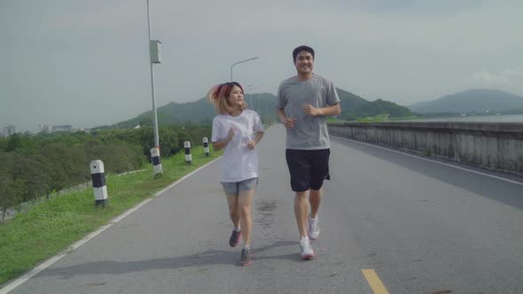 Asian runner couple running and jogging Healthy young sporty sweet couple exercise near lake.