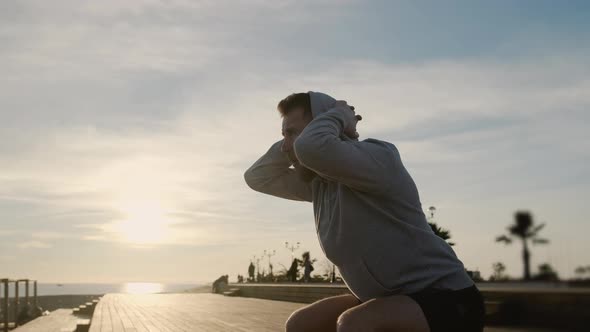 Man Is Crouching on City Embankment in Evening in Sunset Time