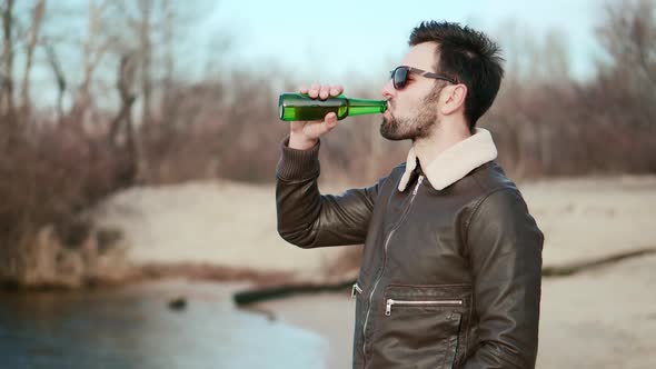 Man Celebrating And Drinking Cold Beer Outdoors From Bottle Enjoying Sunset. Man In Sunglasses.