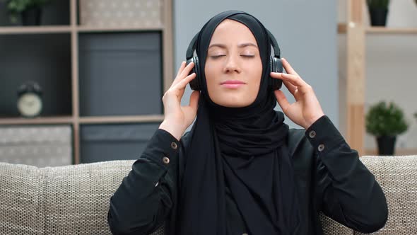 Happy Young Muslim Woman in Black Headscarf Enjoying Audio Sound Wearing Headphones Relaxing