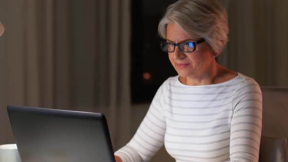 Happy Senior Woman with Laptop at Home in Evening