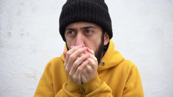 Man In Hipster Beanie Hat And Yellow Hoodie Jacket Rubbing Hand Palms And Freezing In Cold. close up