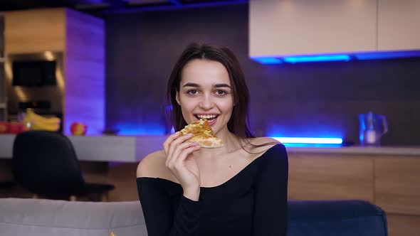 Young Brunette Sitting on the Couch in the Contemporary Room and Eating Pizza, Posing on Camera