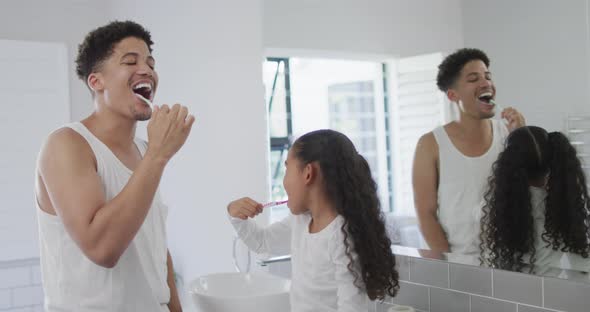 Happy biracial father and daughter washing teeth in bathroom together