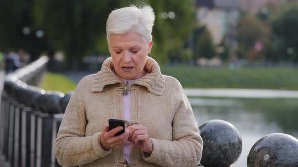 Displeased Retired Woman Looking at Smartphone Screen Outdoor Dissatisfied with Bad News Message
