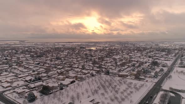 Flying backwards over snow covered city looking at the sunset