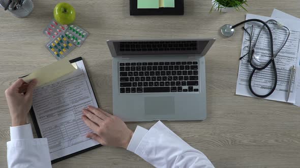 Doctor Looking at Insurance From of Patient and Typing Information on Laptop