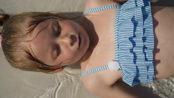 Calm Little Girl Lies in Clear Shallow Pool with Closed Eyelids