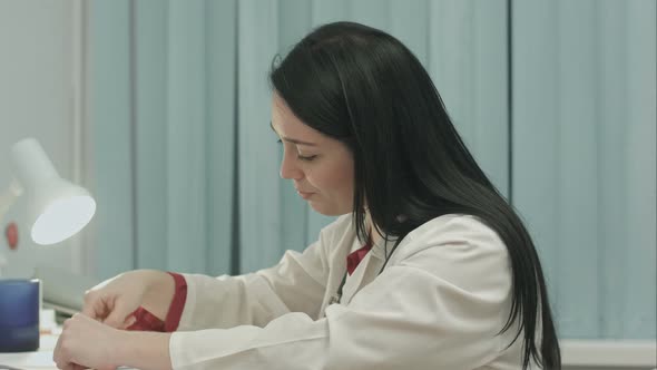 Tired Female Doctor Sits in a Medical Office in the Clinic and Writes Diagnose of Patient